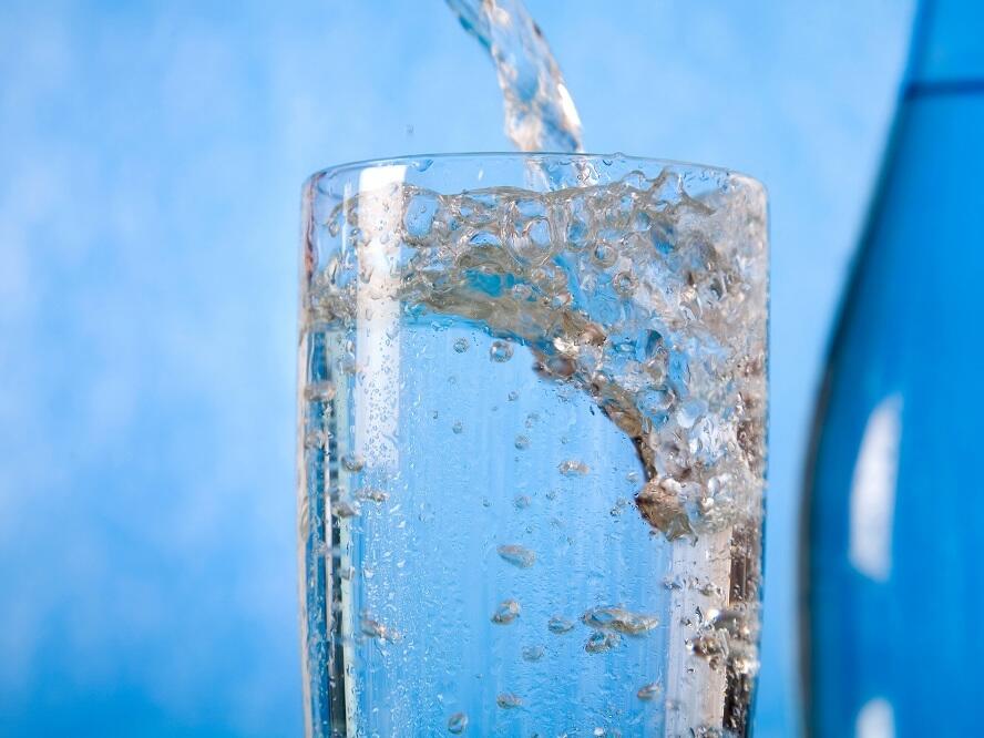 Glas vor blauem Hintergrund wird mit frischem, sprudelndem Trinkwasser befüllt.