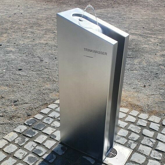 Trinkwassersbrunnen aus rostfreiem Edelstahl mit elliptischer Schräge, Betätigung über Sensortaster.